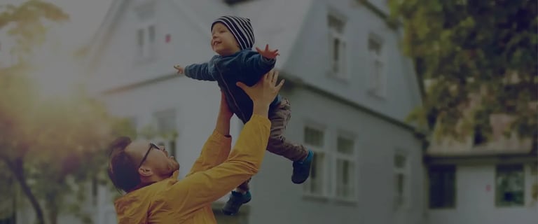 Papà solleva il figlio davanti a una villa protetta con sistema d’allarme Sector Alarm, sicurezza familiare 24/7