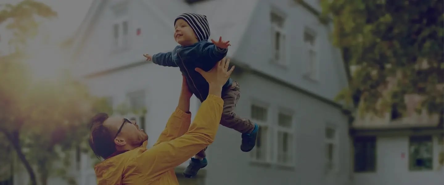 Papà solleva il figlio davanti a una villa protetta con sistema d’allarme Sector Alarm, sicurezza familiare 24/7