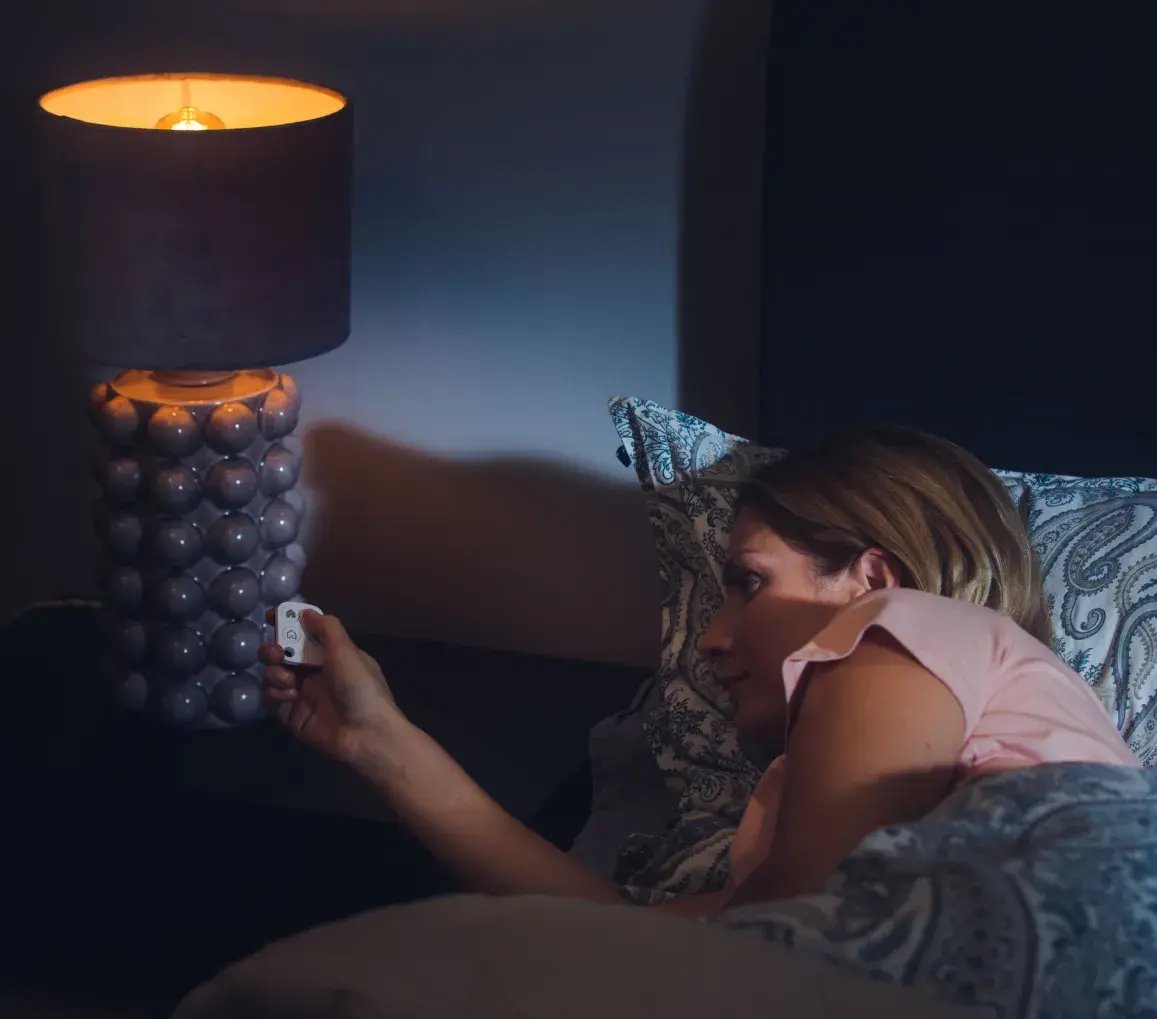 Donna distesa a letto attiva il sistema di sicurezza Sector Alarm con un telecomando Donna distesa a letto attiva il sistema di sicurezza Sector Alarm con un telecomando