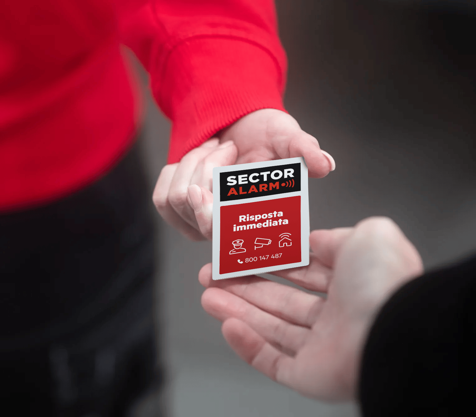 Tecnico Sector Alarm in uniforme rossa consegna un cartello dissuasore a una persona, simbolo di attenzione e protezione condivisa
