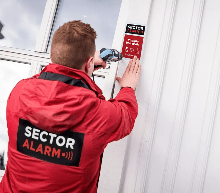 Tecnico Sector Alarm installa un pannello di segnalazione su una parete esterna durante l’installazione del sistema di sicurezza domestica.