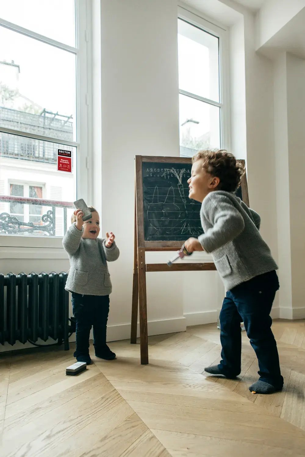 Due bambini giocano in sicurezza vicino a una finestra con sensore Sector Alarm – immagine che trasmette protezione e serenità domestica Due bambini giocano in sicurezza vicino a una finestra con sensore Sector Alarm – immagine che trasmette protezione e serenità domestica